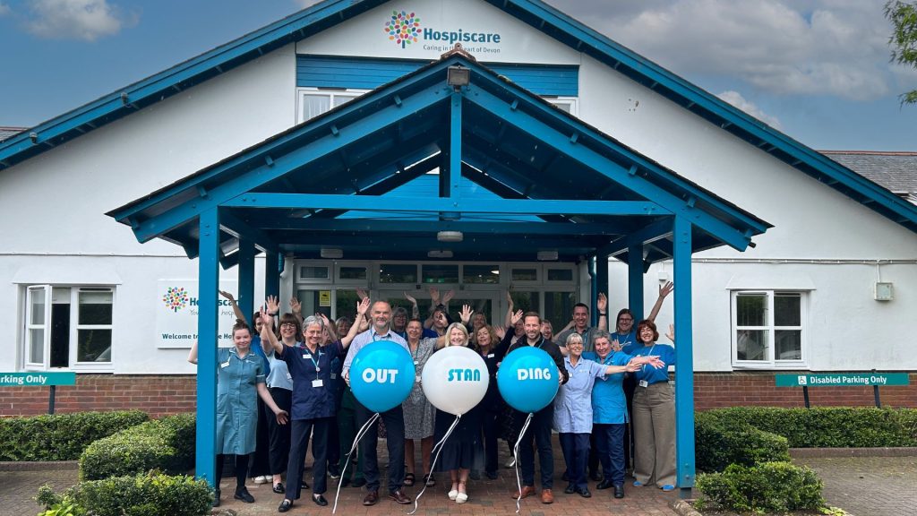 Hospiscare staff and volunteers hold balloons that read 'Outstanding' to celebrate being awarded Outstanding at their recent CQC inspection