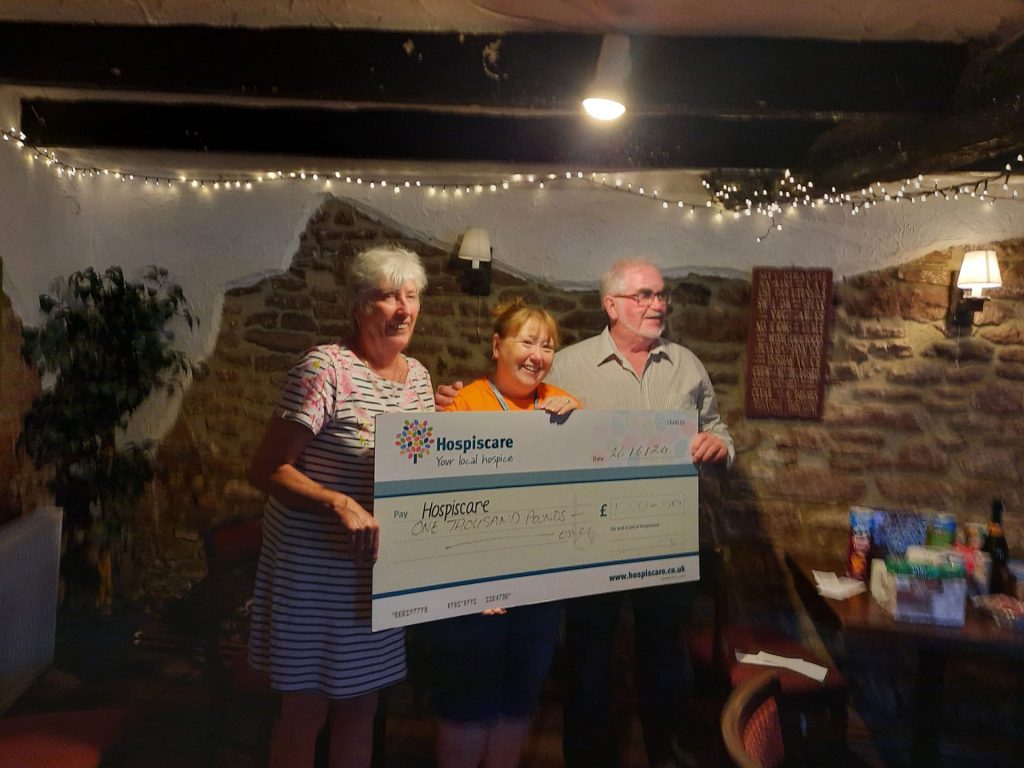 Three people holding a giant cheque under a beam with fairy lights