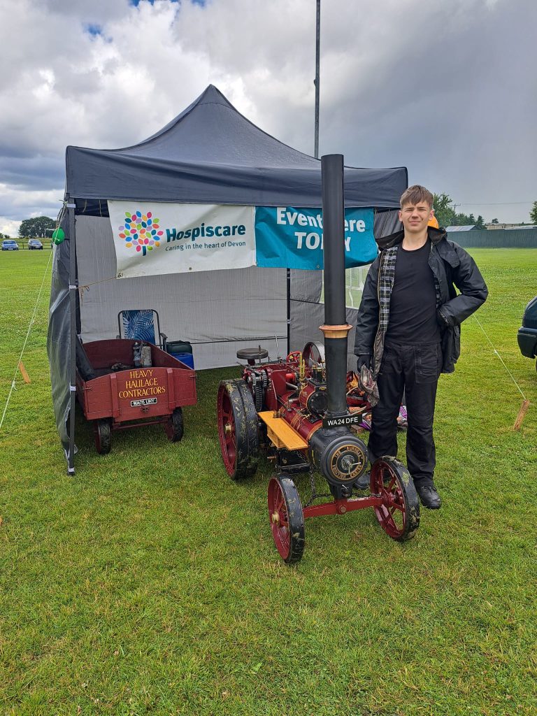 A man stood in front of a small steam engine in a field