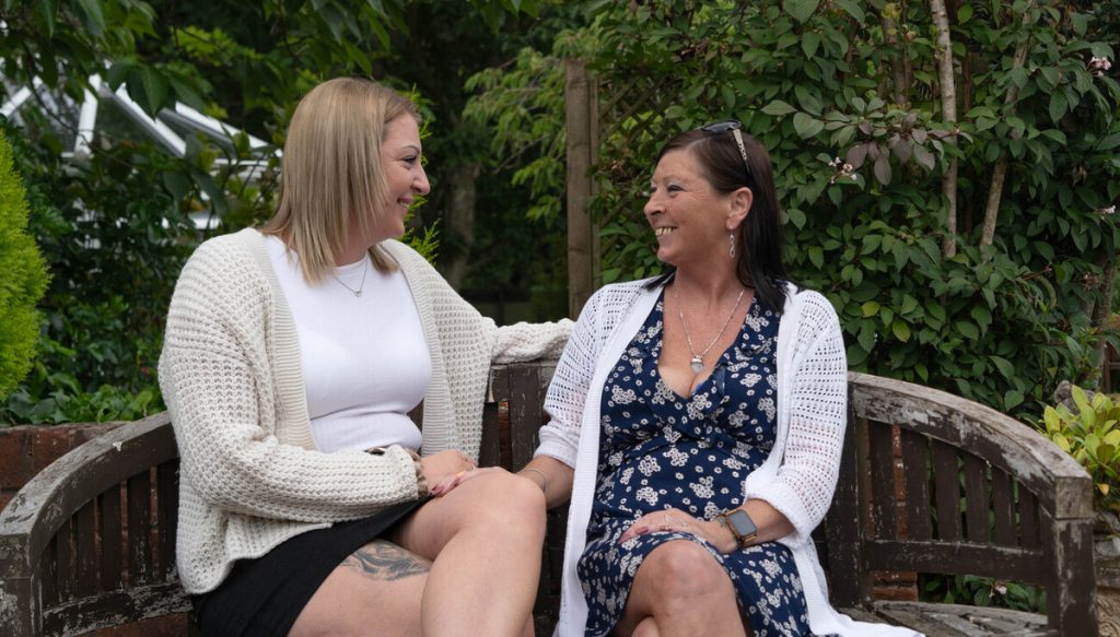 Two women sitting smiling at each other on a garden bench