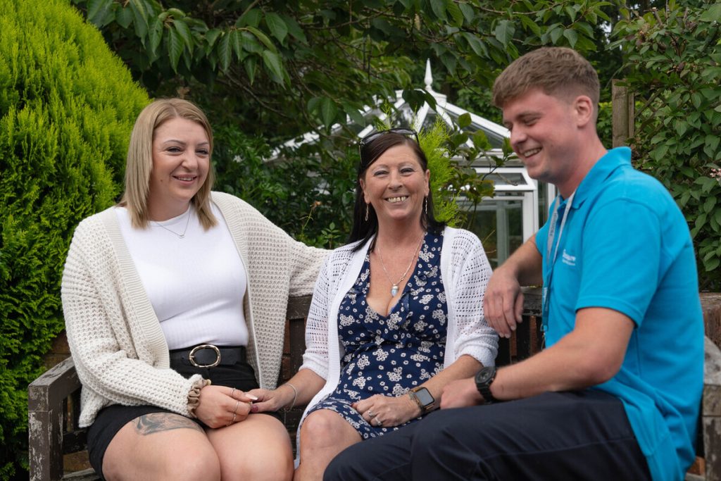 Two women and a man smiling sitting in a garden