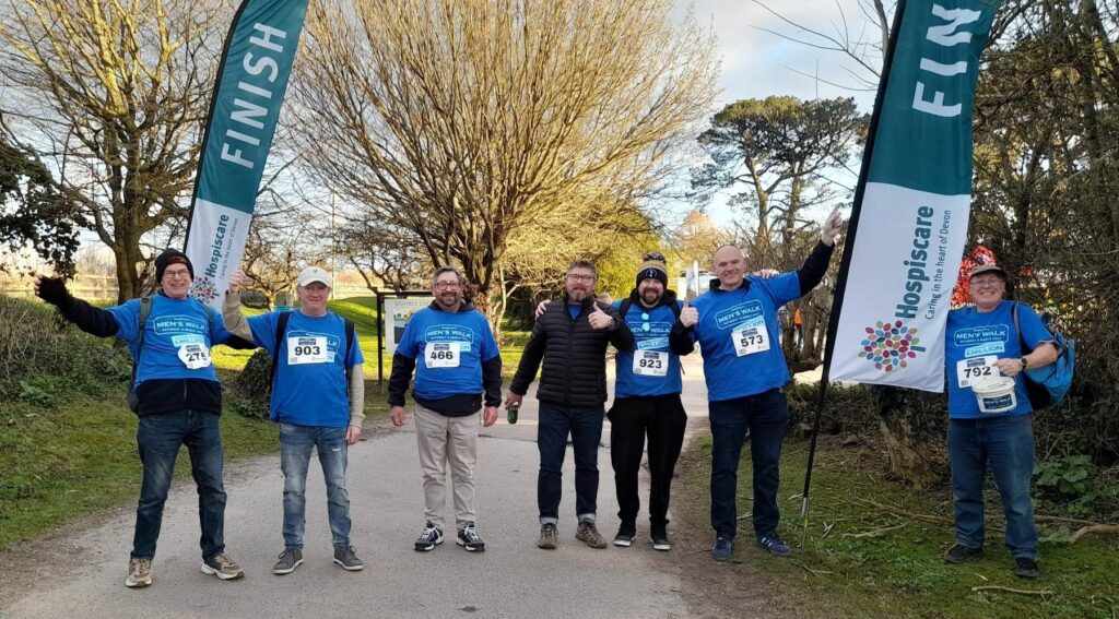 A group of men in blue t-shirts between flags saying finish