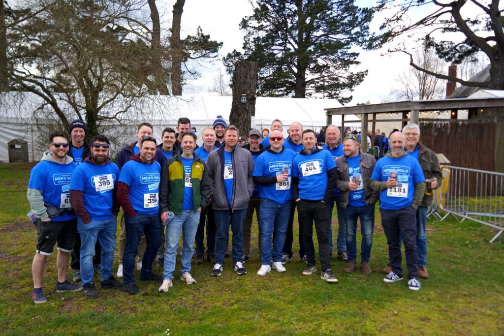 A large group of men smiling, wearing blue t-shirts in a pub garden