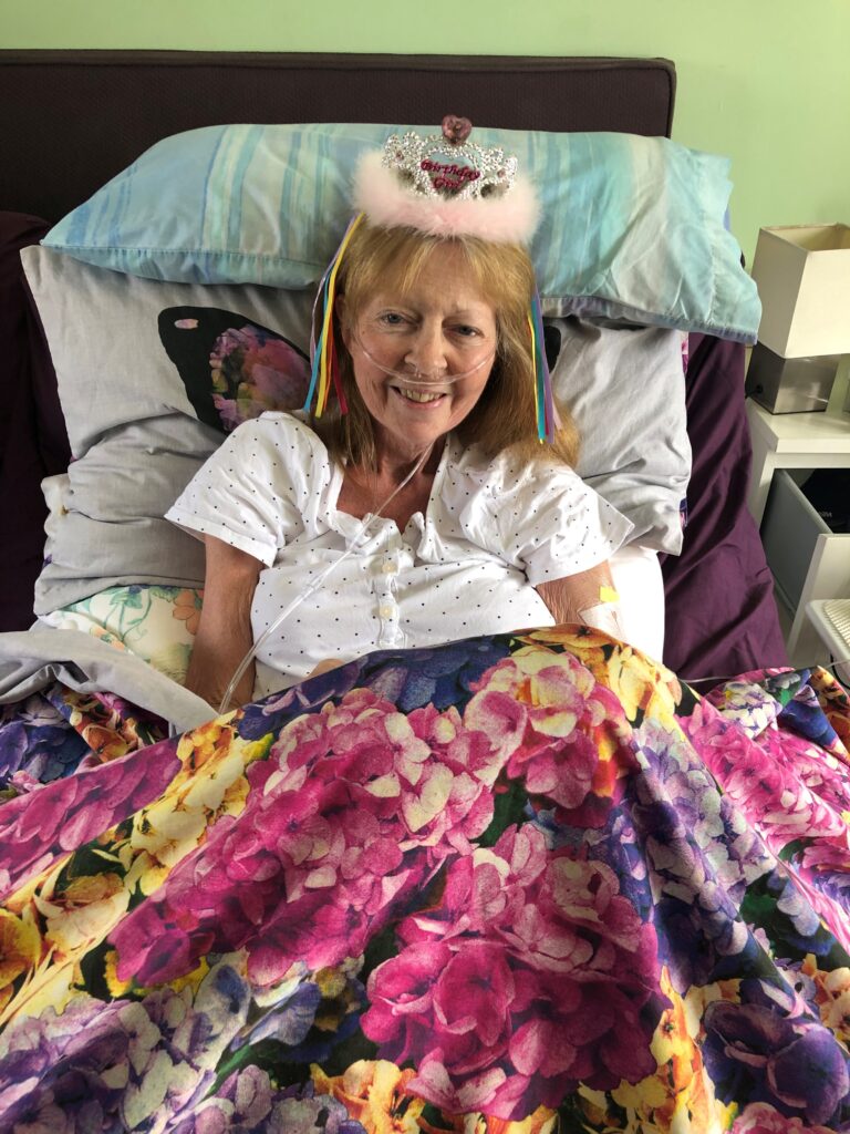 Hospiscare patient Rachel, sat in bed on her birthday wearing a crown decoration on her head and smiling at the camera