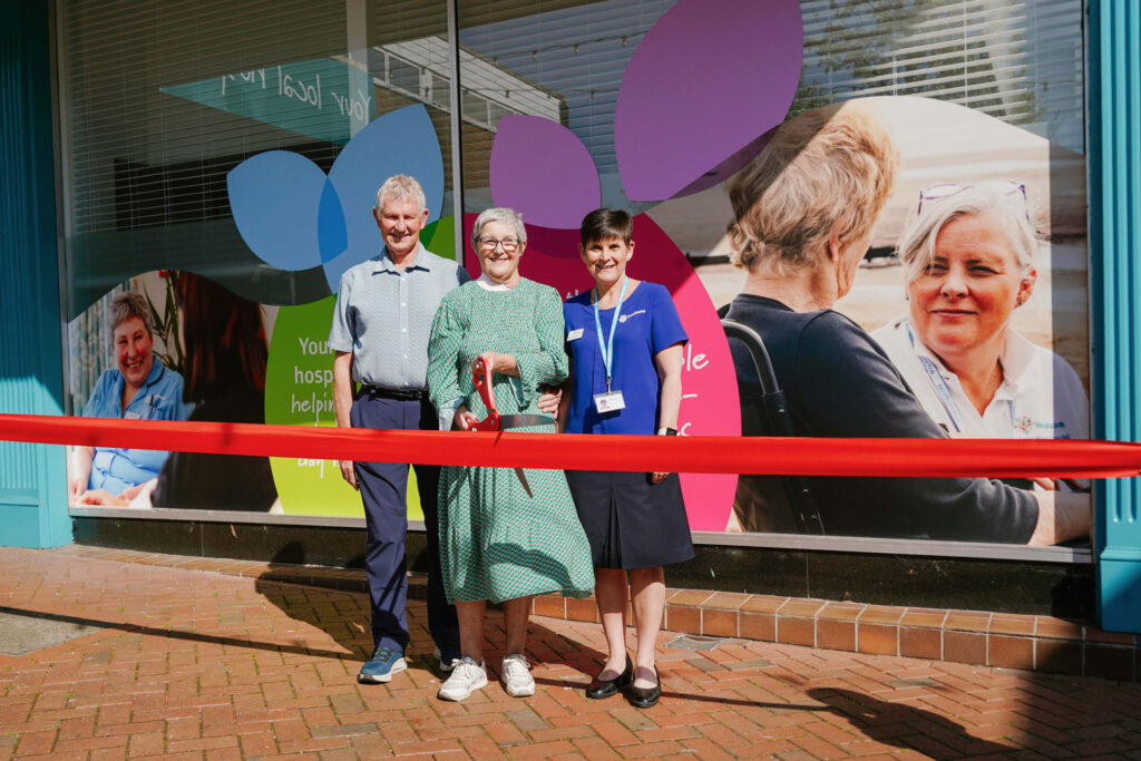 A man and two women standing in front of a building with a red ribbon and large scissors