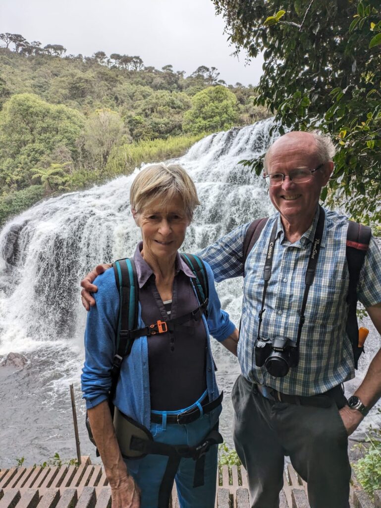 An older woman and man standing in front of a waterfall