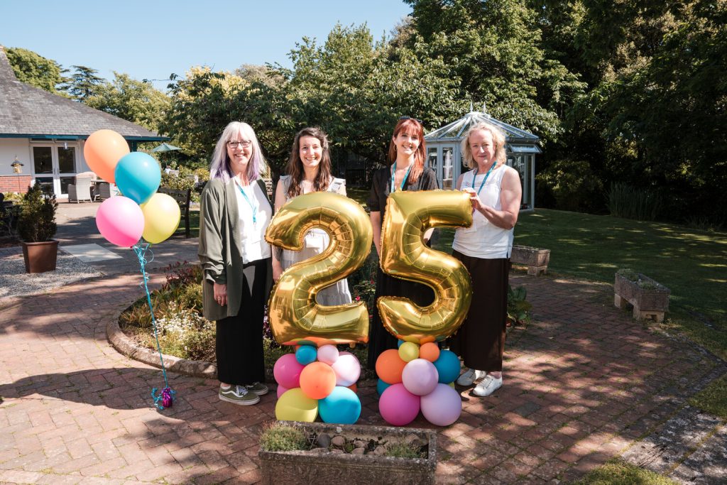 Four women stand behind balloons displaying the number 25 in a garden