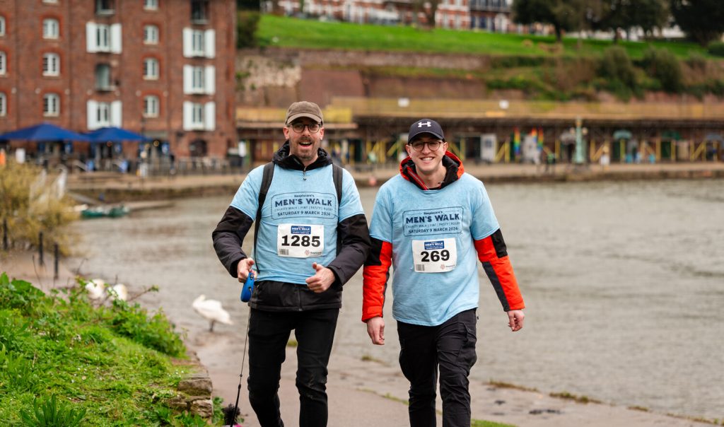 Two men in blue t-shirts walking on a path on Exeter Quayside