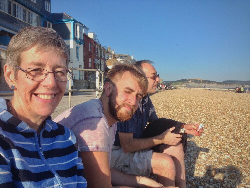A woman and two men sat on a beach in the sun smiling