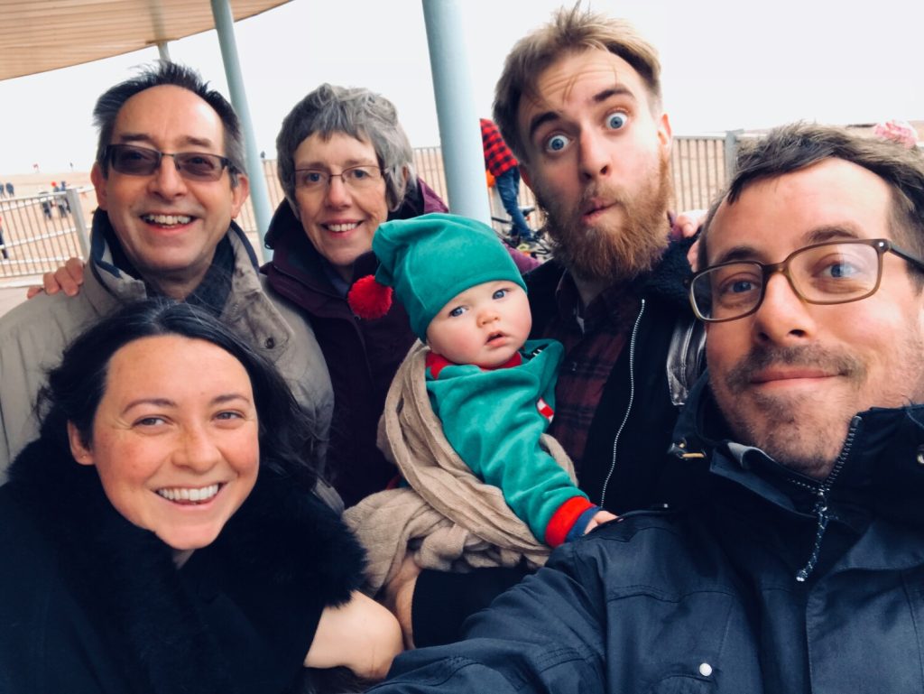 A family group with a baby outdoors smiling at the camera